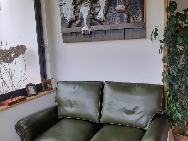 Canapé Club 2 places dossier haut cuir vert anglais à côté d'une plante verte