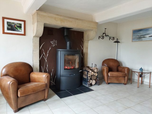 2 fauteuils Club cuir Rochembeau de chaque côté d'un poêle à bois dans une pièce claire en carrelage blanc-crème