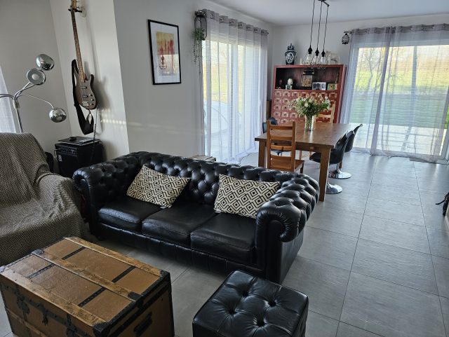Un canapé Chesterfield en cuir noir et un pouf capitonné en cuir noir de marque Rochembeau dans un salon devant une malle en bois