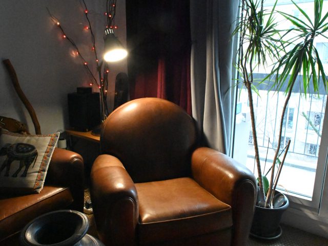 un fauteuil Club cuir marron Rochembeau dans un salon sur un tapis rouge à côté d'une fenêtre baie vitrée