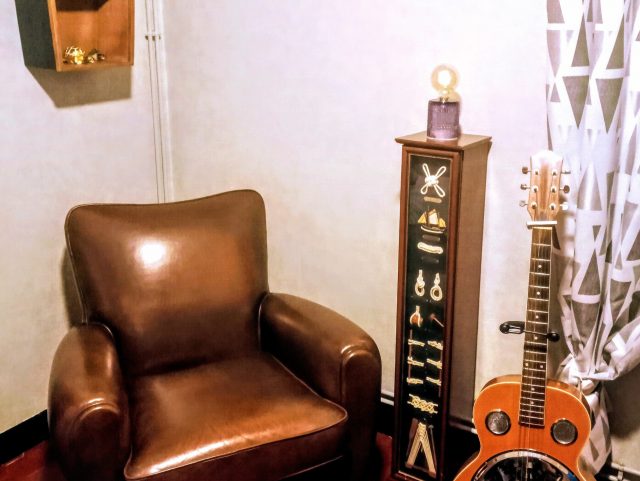 Un fauteuil Club SHEFFIELD cuir marron foncé Rochembeau à côté d'une guitare basse