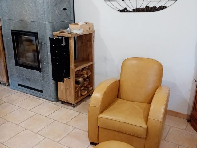 Un fauteuil Club et un pouf rond cuir jaune miel Rochembeau à côté d'un poêle à bois de masse 