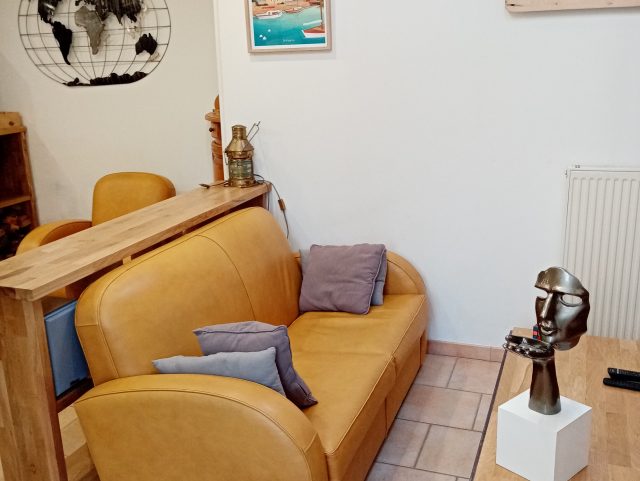 Canapé 2 places Club cuir jaune miel Rochembeau devant un table basse et sculpture main visage