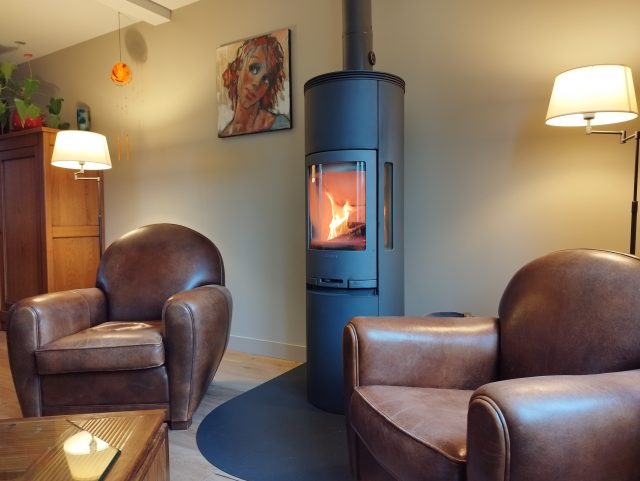 2 fauteuils Club cuir marron Rochembeau dans un salon et proche d'un poêle à bois design en métal gris brossé