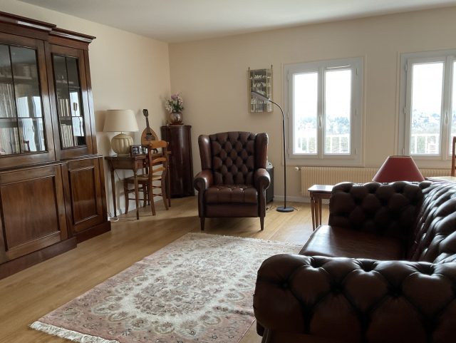 Fauteuil à oreilles et assise capitonnée et canapé Chesterfield cuir marron Rochembeau dans un salon