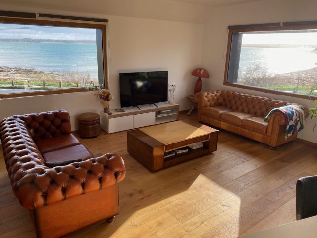 Deux canapés Chesterfield cuir Rochembeau autour d'une table basse et 2 baies vitrées donnant sur la mer bretonne