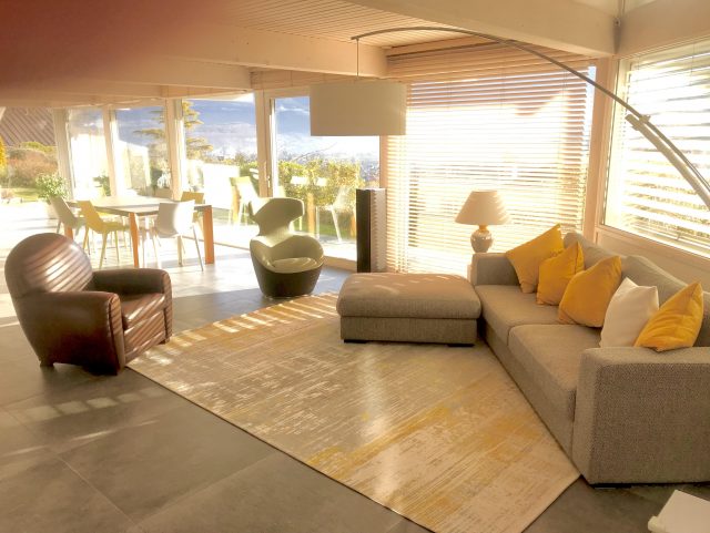 Fauteuil Club  cuir marron foncé Rochembeau devant un canapé tissus dans un salon très ensoleillé