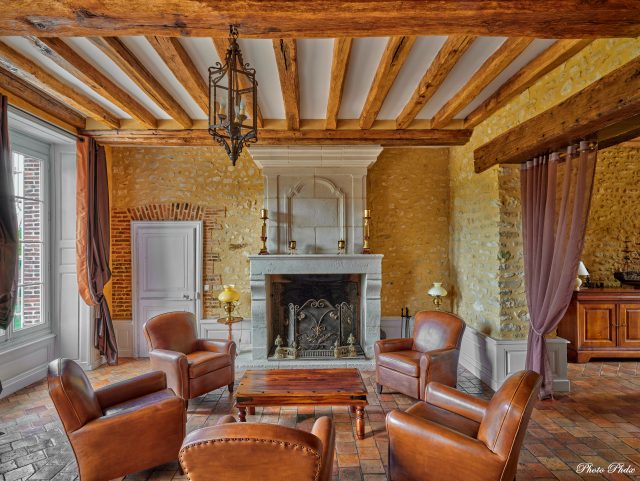 5 fauteuils Club cuir Rochembeau dans un salon autour d'une table basse en bois, devant un cheminée, murs en pierres et poutres en bois