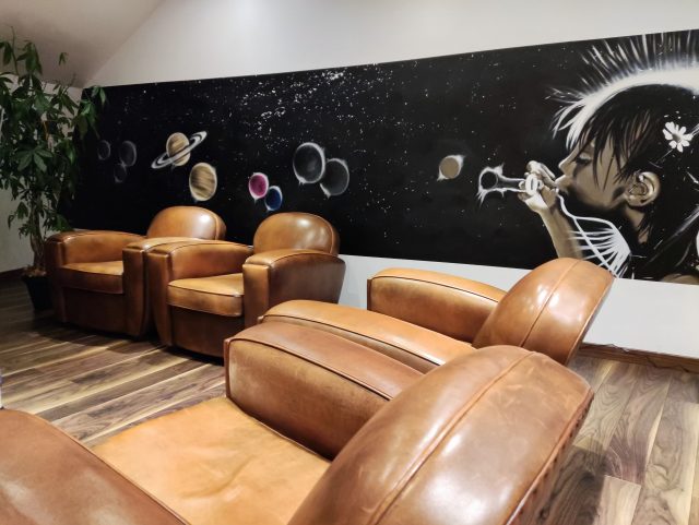 4 fauteuils Club cuir marron dans un salon et devant une grande fresque murale