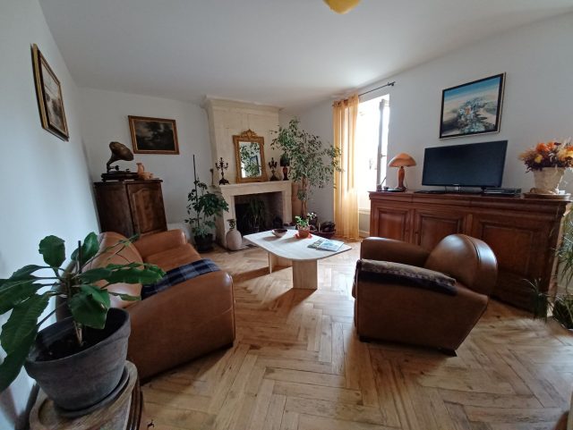 Un canapé Club et un fauteuil Club cuir marron dans un salon sur parquet massif bois devant une télévision écran plat